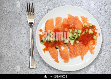 Lachs, roter Kaviar, Rucola und frischer Gurkensalat auf grauem Hintergrund Stockfoto