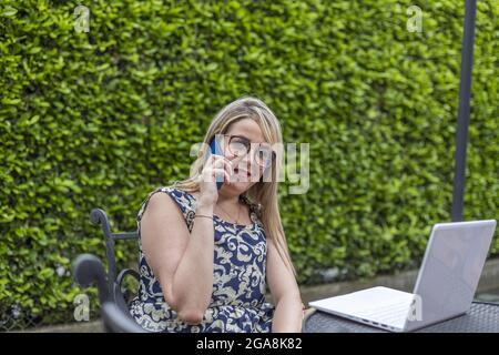Kaukasische blonde Frau, die während der Arbeit im Garten auf ihrem Mobiltelefon spricht Stockfoto