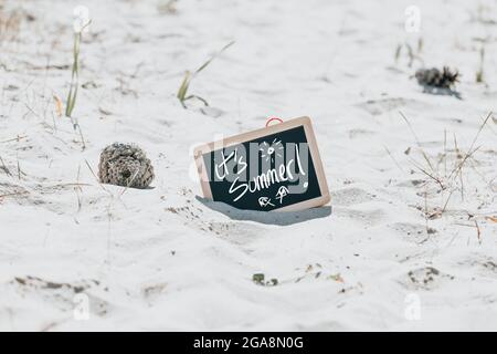 Kleine Tafel mit Holzrahmen und einem „IT's Summer!“ Schreiben am Sandstrand Stockfoto