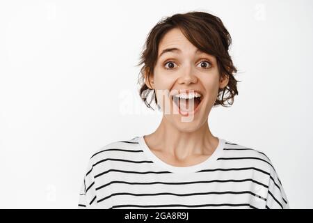 Nahaufnahme Porträt der überrascht und erstaunt Brünette Frau, keuchend fasziniert, Blick erstaunt, stehen vor weißem Hintergrund Stockfoto