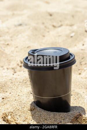 Schwarze Einweg-Kaffeetasse aus Kunststoff auf dem Sand Stockfoto