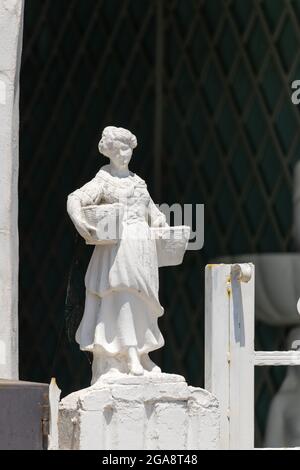 Weiße Statue am Tor eines Mädchens in einem Kleid mit zwei Körben Stockfoto