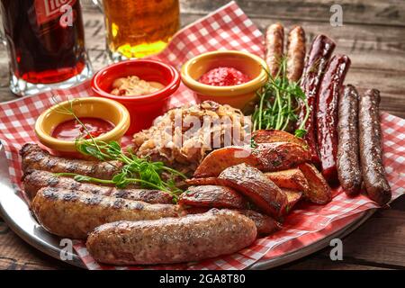 Bierset mit gegrillten Würstchen mit gedünstetem Kohl, Kartoffelkeilen und Saucen Stockfoto