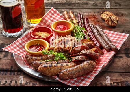 Gegrillte Würstchen mit Kartoffelkeilen, gedünstetem Kohl und Saucen als Biersnack Stockfoto