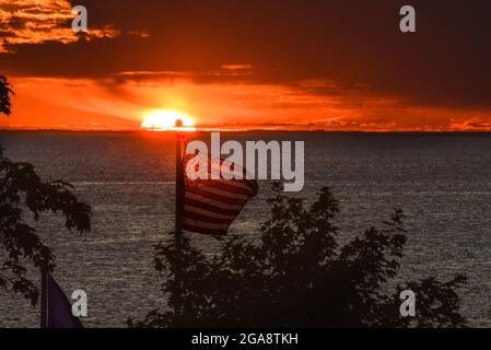 Die amerikanische Flagge flattert im Wind mit einem herrlichen Sonnenuntergang über Green Bay (Lake Michigan), der vom Park in Egg Harbor, Door County, Wisconsin, USA aus gesehen wird Stockfoto