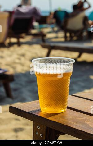 Bier in einem durchsichtigen Plastikglas, das an einem sonnigen Sommertag auf was gelegt wird