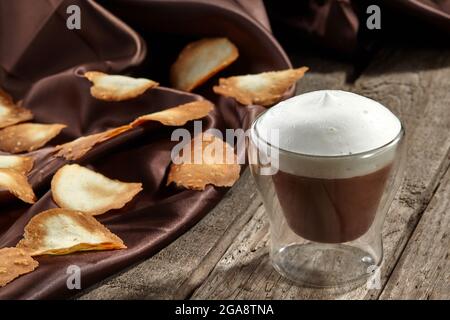 Schokoladenmousse mit aufgeschäumter Milch im Glas mit süßen knusprigen Chips Stockfoto