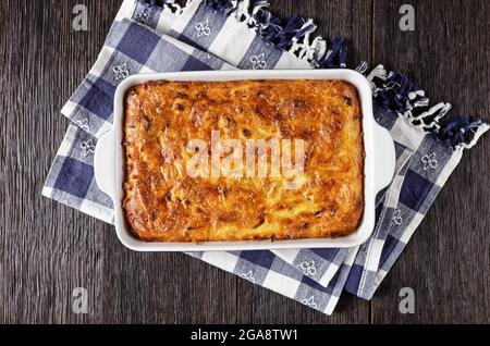 Pikante Kartoffel-kugel, gebackener Pudding oder Auflauf geriebener Kartoffel in einer Auflaufform auf einem Holztisch, jüdisches Feiertagsrezept, flaches Lay Stockfoto