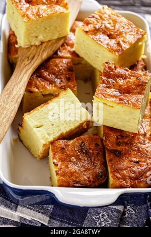 kartoffelkugel, gebackener Pudding oder Auflauf geriebener Kartoffeln, die in Portionen in einer Auflaufform auf einem Holztisch geschnitten werden, jüdisches Feiertagsrezept Stockfoto