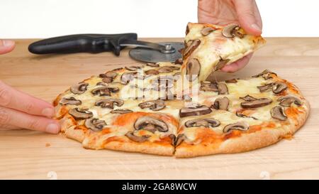 Crimini Pilzpizza mit Mozzarella-Käse und Tomatensauce aus nächster Nähe auf Holzschneidebrett auf weißem Hintergrund, Frauenhände Stockfoto