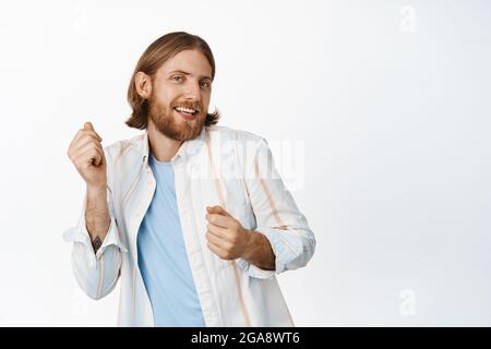 Porträt eines hübschen blonden bärtigen Kerls, tanzend sorglos, lächelnd freudig, stehend in lässigem Outfit vor weißem Hintergrund Stockfoto