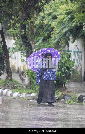 Dhaka, Bangladesch. Juli 2021. Eine Frau sah, wie sie während eines regnerischen Tages inmitten der covid-19-Sperre einen Regenschirm hielt, während sie auf einer leeren und verlassenen Straße ging.das Land wurde streng gesperrt und schwerer Monsunregen verursachte extreme Wassereinschläge in den meisten Gebieten der Stadt Dhaka. Die Straßen waren unter Wasser, was die Reise langsam und gefährlich machte. (Bild: © Sazzad Hossain/SOPA Images via ZUMA Press Wire) Stockfoto