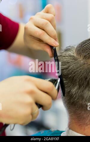 Der Friseur schneidet dem Mann die Haare mit einem Haarschneider und Kamm. Kurzer Haarschnitt für Männer. Nahaufnahme. Stockfoto