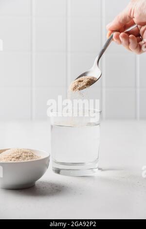 Frau fügt auf weißem Hintergrund Psylliumfaser zu Glas Wasser hinzu. Superfood für gesunden Darm und glutenfreie Ernährung. Stockfoto