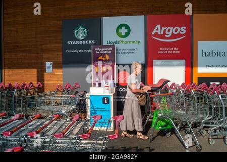 Taplow, Buckinghamshire, Großbritannien. 22. Juli 2021. Eine Dame bekommt ihren Wagen, nachdem sie ihn an der Desinfektionsstation desinfiziert hat. Nach der Lockdown-Aufhebung der Covid-19 am Montag hat Sainsbury's neue Schilder vor seinem Geschäft, auf denen die Kunden aufgefordert werden, Masken zu tragen, wenn sie können. Quelle: Maureen McLean/Alamy Stockfoto