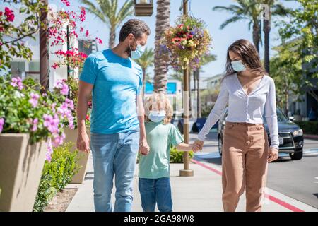 Junge Familie von Mutter Vater und Kind tragen Schutzmaske zu Fuß im Freien, covid 19 Stockfoto