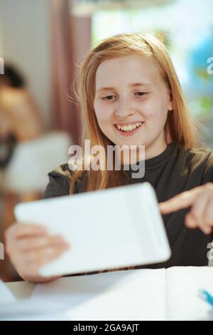 Glückliches modernes Kind in grauem Hemd mit Tablet-PC Heimschooling zu Hause an sonnigen Tagen. Stockfoto