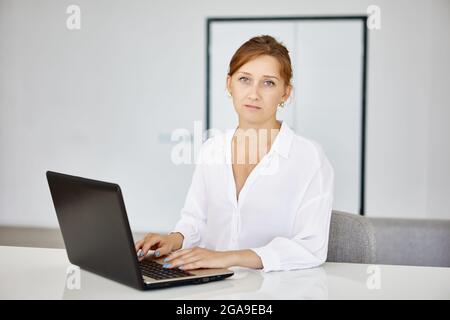 Seriöse Frau im Hemd mit Laptop während der Fernarbeit. Stockfoto