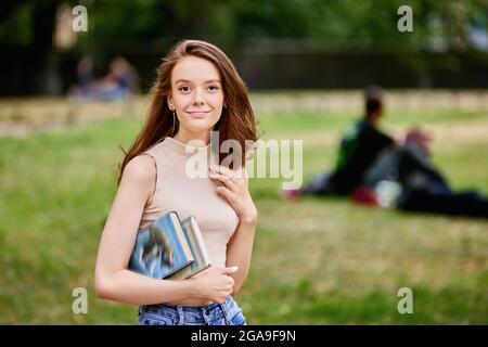 Glückliche anmutige Frau mit Büchern in den Händen draußen. Stockfoto