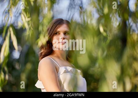 Nachdenkliche junge weibliche Spaziergänge im Stadtgarten im Sommerkleid. Stockfoto