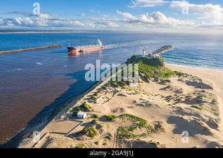 Eine Luftaufnahme des Nobbys Lighthouse und des Newcastle Harbour mit großem Schiff, das in den Hafen eindringt. Newcastle ist einer der größten Kohleexporthäfen der Welt Stockfoto