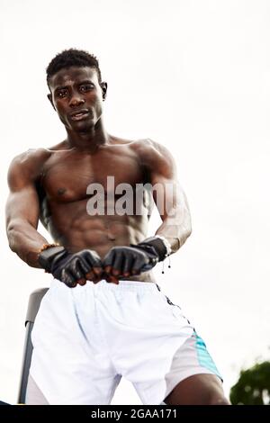 Muskulöser schwarzer Profi-Boxer schwitzt in Handschuhen beim Boxtraining im Freien, junger afroamerikanischer Boxer beim Training auf dem Straßenspielplatz. Stockfoto