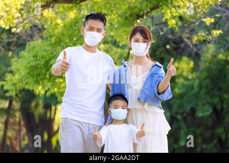 Glückliche Familie, die medizinische Masken trug, um sich zu schützen und die Daumen hoch zu zeigen Stockfoto