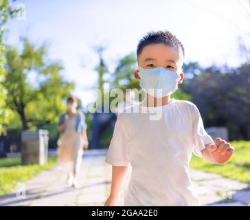 Glücklicher kleiner Junge mit medizinischer Maske und Spaziergang mit den Eltern im Park Stockfoto