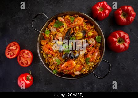 Traditionelle spanische Paella mit Meeresfrüchten und Tomaten auf schwarzem Hintergrund Stockfoto