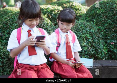 asiatischer Grundschüler mit Mobiltelefon im Schulpark Stockfoto