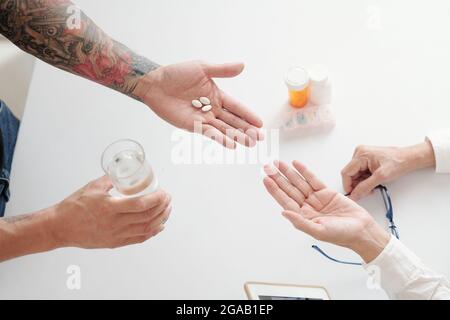 Nahaufnahme eines Mannes, der seiner Mutter Pillen und ein Glas Wasser gab, während sie am Tisch saß Stockfoto