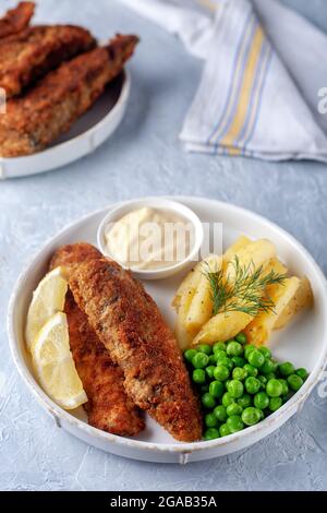 Gebratener Fisch mit gebratenen Kartoffeln, grünen Erbsen und Zitrone Stockfoto