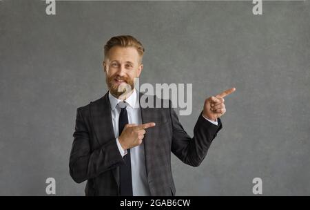 Ein Geschäftsmann, der vor grauem Hintergrund steht, weist beide Zeigefinger weg Stockfoto