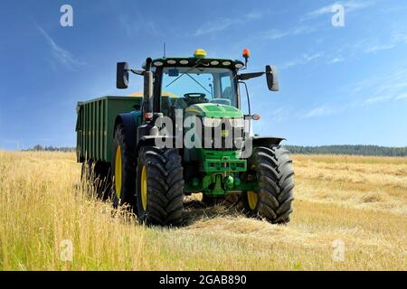 John Deere 6155R Traktor und Kire Anhänger voller geerntetem Weizen auf dem Feld an einem schönen Tag. Salo, Finnland. 25. Juli 2021. Stockfoto