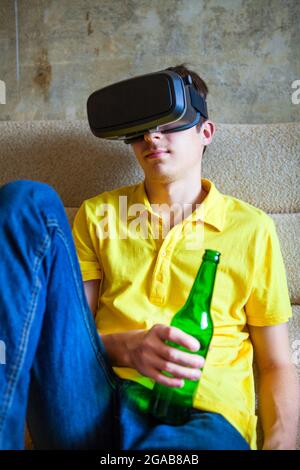 Junger Mann in VR-Brille hält eine Flasche Bier auf dem Sofa Stockfoto