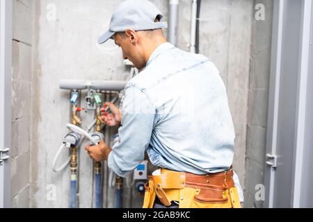 Männlicher Klempner prüft Rohre für zentrale heiß- und Kaltwasserversorgung der Wohnung Stockfoto