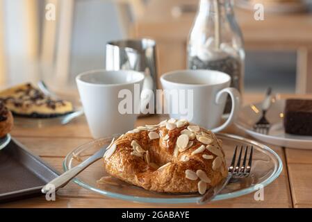 Süßer Croissant-Mandel-Kellner mit Americano und Latte und Schokoladenherb auf dem Holzschreibtisch im Café Stockfoto