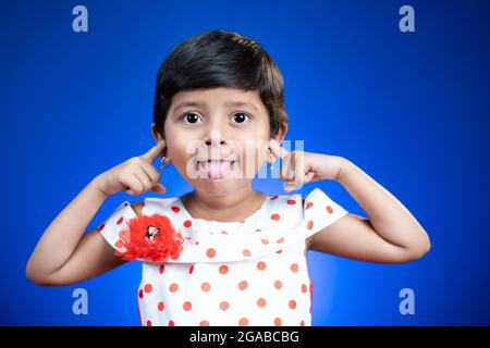 Kleine Mädchen mit der Zunge raus oder grimazing Tanz auf blauem Hintergrund - glücklich, fröhlich und verrückt Kinder Konzept. Stockfoto