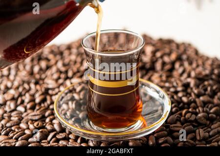 Mann hält und gießt Kaffee in eine Glastasse auf gerösteten Kaffeebohnen Stockfoto
