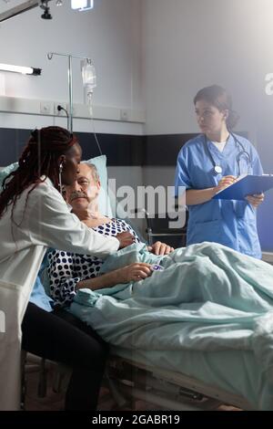 Kardiologe in Uniform untersucht Senior Mann während der medizinischen Besuch, hören Herz mit Stehoskop, um Herz zu hören. Mann mit kranken Lungen, der durch den Sauerstoffschlauch atmet und das Oximeter am Finger befestigt ist. Stockfoto