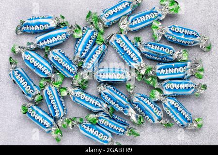 Candy Bounty Mini der amerikanischen Firma. Ein Haufen eingewickelter Schokoladentafeln mit Kokosnuss auf grauem Hintergrund. Süßwarenprodukt mit Logo. Illustrati Stockfoto