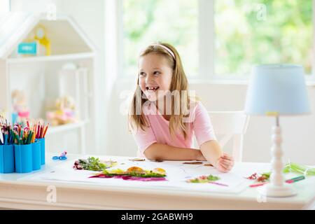 Kind schafft Bild mit bunten Blättern. Kunst und Kunsthandwerk für Kinder. Kleines Mädchen macht Collage Bild mit Regenbogenpflanzen Blatt. Hausaufgaben für die Biologie Stockfoto