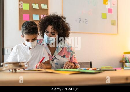 Lehrerin mit Kinderzeichnung im Vorschulunterricht, während sie Gesichtsschutzmaske während einer Corona-Virus-Pandemie trägt Stockfoto