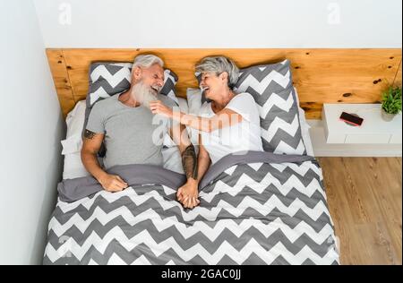 Glückliches Senioren-Paar, das zusammen lacht, während es im Bett unter Decken liegt - älterer Lebensstil und Liebesbeziehung Konzept Stockfoto