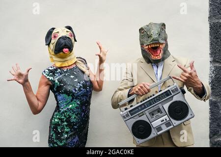 Glückliches Seniorenpaar mit Spaß tragen Hund und t-rex Maske - Ältere Menschen feiern Karnevalsferien beim Tanzen und Musik hören Stockfoto