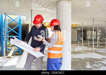 Architekt und Handwerker betrachten gemeinsam einen Bauplan auf einer Baustelle im Rohbau Stockfoto