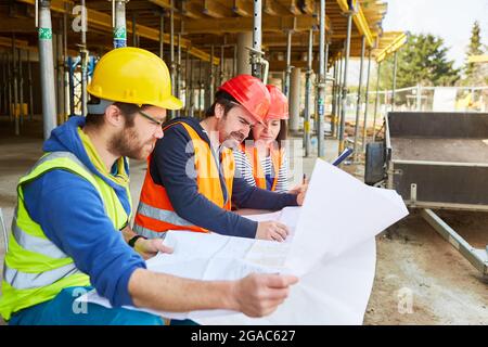 Handwerker-Team und Architekt auf der Rohbaustelle mit Blaupause für das neue Hausgebäude Stockfoto