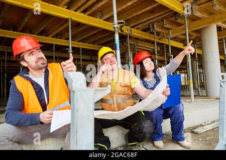 Handwerker und Architekt als Team mit Bauzeichnungen bei der Planung auf der Baustelle im Rohbau Stockfoto