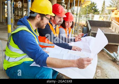 Arbeiter und Handwerker diskutieren im Team mit dem Architekten den Grundriß auf der Baustelle im Rohbau Stockfoto