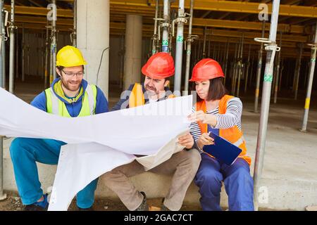 Handwerker-Team und Architekt mit Blaupause bei der Planung der Arbeiten im Rohbau der Baustelle Stockfoto